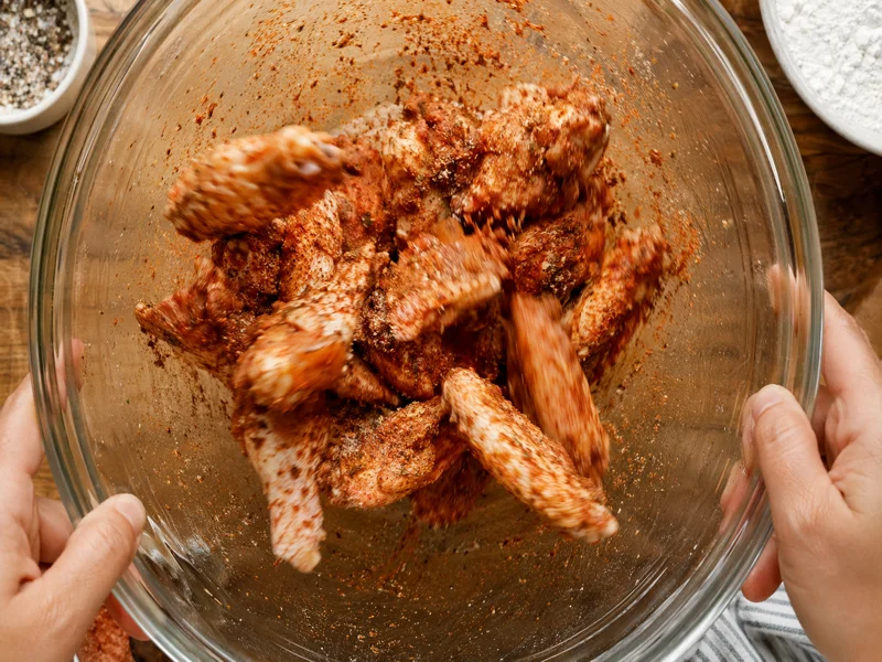 Seasoning raw chicken wings with dry rub spices in a mixing bowl
