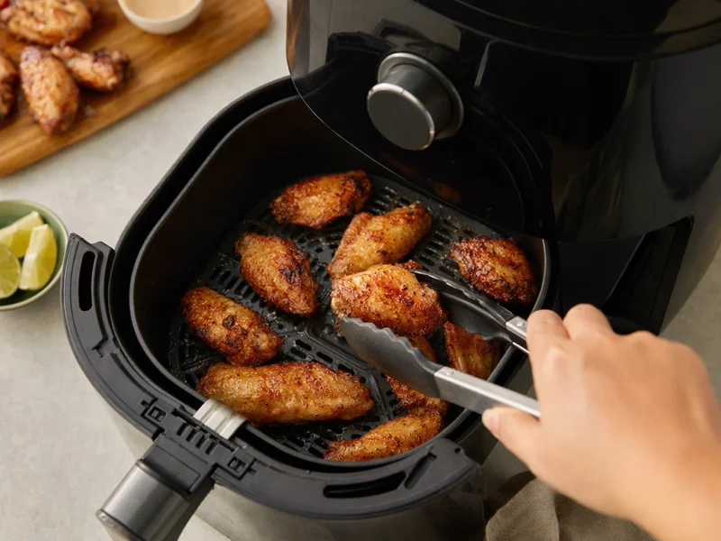 Golden brown chicken wings being flipped in air fryer basket halfway through cooking