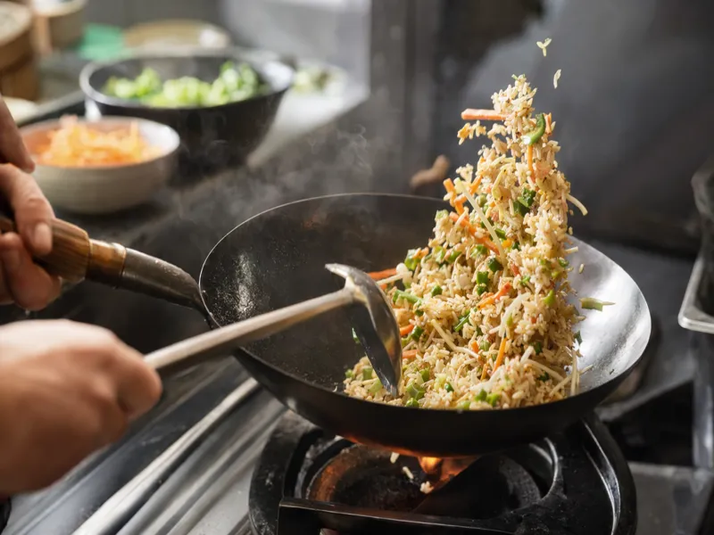 Tossing chilled rice with vegetables in a wok over high heat with slight charring